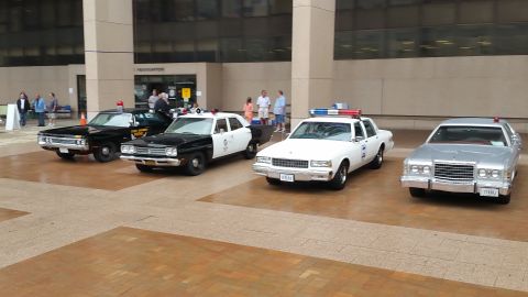 1991 Ford LTD Crown Victoria - Photograph of four classic police cruisers parked in a row on a brick plaza, not a technical document.