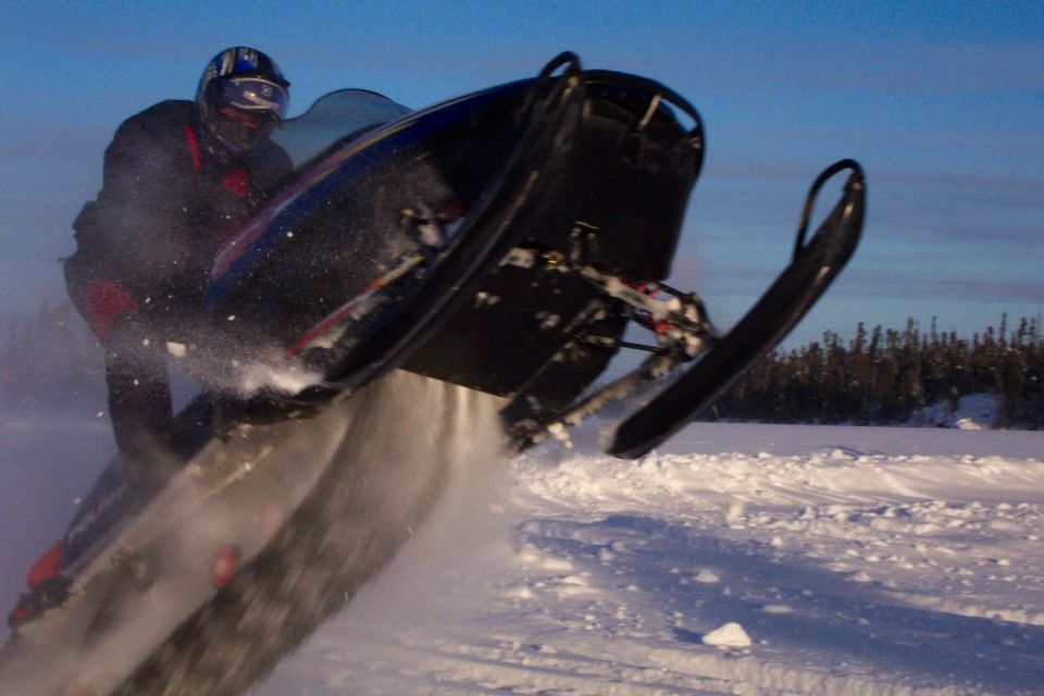 Rider jumping a dark snowmobile off snow into blue sky
