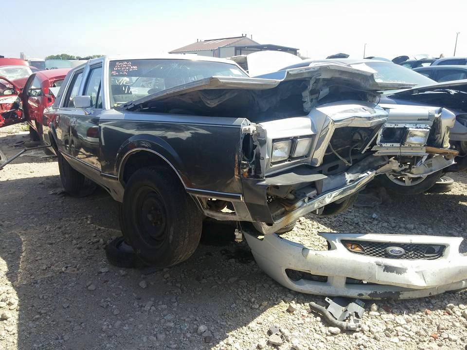 Front-collision-damaged dark Lincoln sedan in a salvage yard