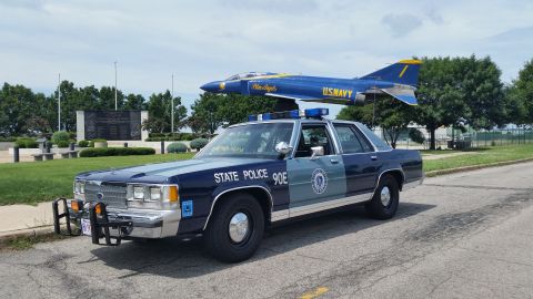 1991 Ford LTD Crown Victoria - Photograph of a Massachusetts State Police Ford cruiser parked near a Navy Blue Angels jet display, not a technical document.
