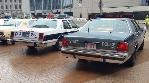 1991 Ford LTD Crown Victoria - Photograph of a blue State Police cruiser next to white emergency vehicles, not a technical document.