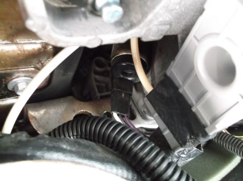 1999 Mercury Grand Marquis - A close-up view shows a black electrical connector attached to a sensor, with a ribbed black conduit and a beige wire running nearby. The c…