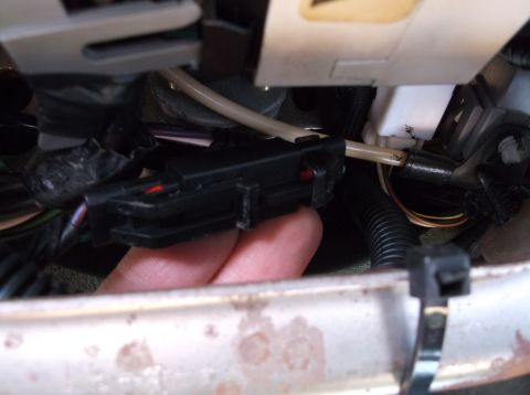 1999 Mercury Grand Marquis - A hand is holding a black electrical connector with red and green wires visible. The connector is attached to a bundle of wires and a beige…