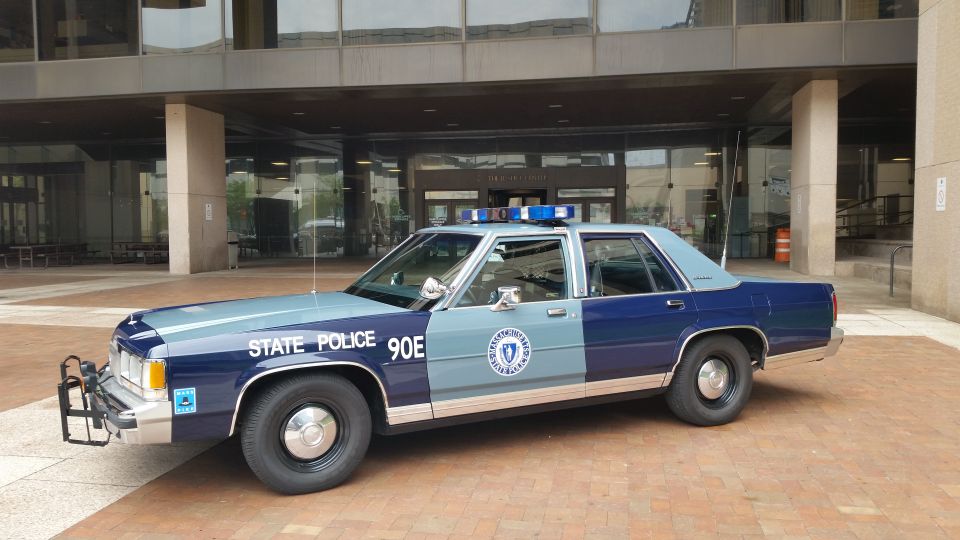 Blue Massachusetts State Police Ford cruiser parked outside building entrance