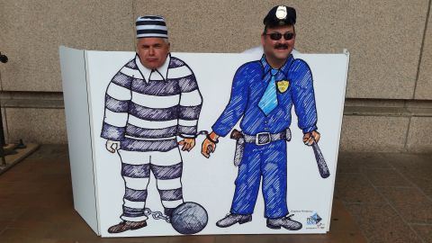 1991 Ford LTD Crown Victoria - Photo of a novelty face-cutout photo board with cartoon prisoner and police officer characters.