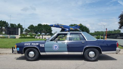 1991 Ford LTD Crown Victoria - Photo of a Massachusetts State Police Ford Crown Victoria cruiser, unit 90E, in profile near a Blue Angels display jet.