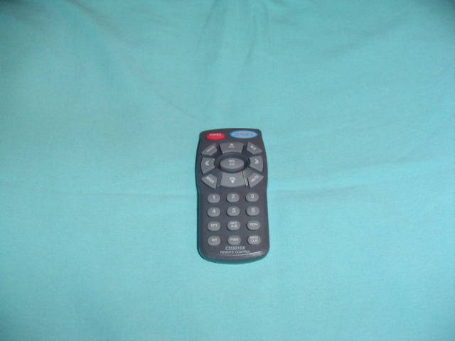 Gray Jensen CD3010X car stereo remote control on teal fabric