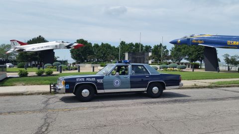 1991 Ford LTD Crown Victoria - Photograph of a vintage Massachusetts State Police sedan parked in front of static military jet aircraft displays.