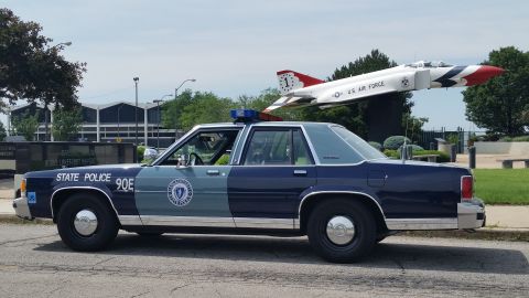 1991 Ford LTD Crown Victoria - Photograph of a State Police sedan parked beside a static U.S. Air Force fighter jet display.