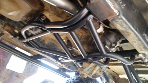 1988 Ford Bronco - The underside of a vehicle shows a custom black metal roll cage or protection structure welded to the frame, surrounding the transmission a…