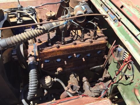 1946 Jeep Willys - A close-up view of a rusty, vintage inline-four engine, likely from a Jeep CJ5, showing spark plug wires, hoses, and a fuse box with red an…