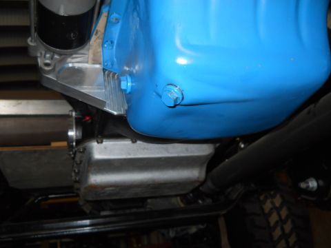 1992 Ford Bronco - A close-up view of a blue oil pan with a silver drain plug, attached to a vehicle's engine. Below the blue oil pan is a silver transmission…