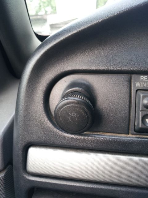 1995 Ford Bronco - A close-up view of a knob with a light bulb icon on a dark gray dashboard, next to a button labeled "REAR WIND".