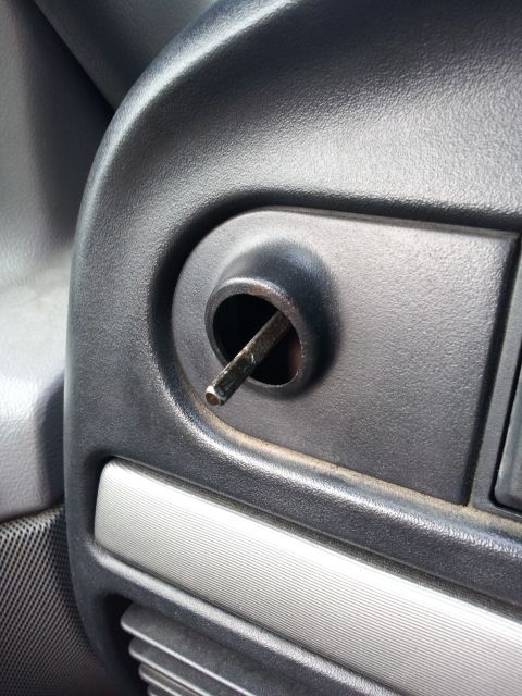 1995 Ford Bronco - A close-up view shows a metal rod inserted into a circular opening on the black interior dashboard of a vehicle. A textured silver trim pie…