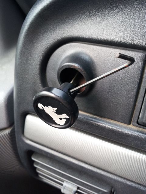 1995 Ford Bronco - A close-up view of a black knob with a white horse emblem, likely for a choke or starter, inserted into a vehicle's dashboard. A thin metal…
