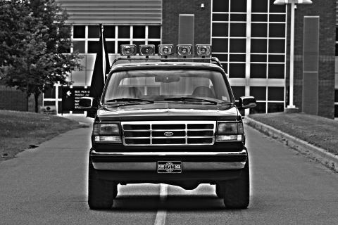1995 Ford Bronco - Front view of a black Ford Bronco with a light bar and five spotlights mounted on the roof. A POW MIA license plate is visible on the front…