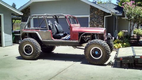 1985 Jeep CJ7 - A custom-built, red Jeep CJ7 is parked in a driveway next to a house. The vehicle features a roll cage, large off-road tires, and exposed e…