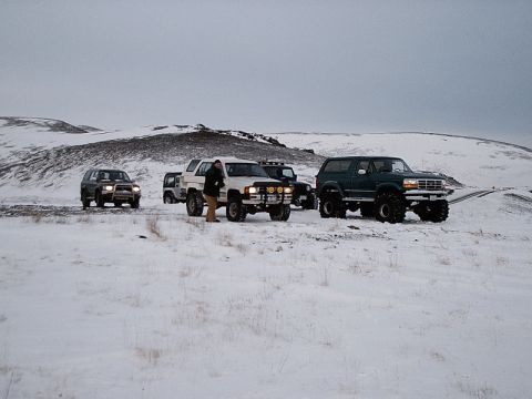 1996 Ford Bronco - Several off-road vehicles are parked in a snowy landscape under an overcast sky.