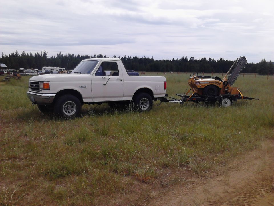 1990 Ford Bronco towing a yellow trencher
