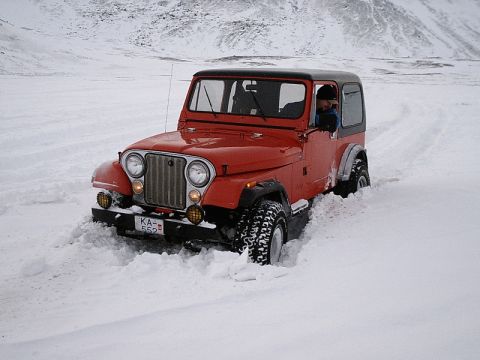 1996 Ford Bronco - A red Jeep CJ-7 navigates a snowy landscape, its grille and front tires clearly visible.