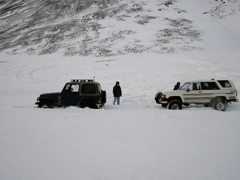1996 Ford Bronco - Two off-road vehicles are stuck in a snowy landscape, with people standing around them.