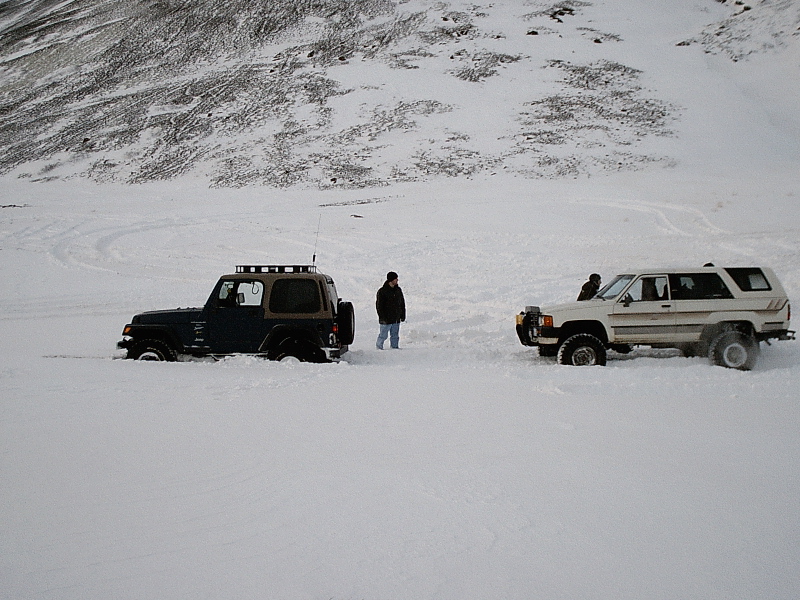 Dark Jeep and white SUV stuck in deep snow with a person standing between them