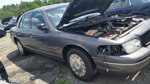 2001 Ford Crown Victoria - Photo of a gray Ford Crown Victoria sedan with its hood raised in an outdoor salvage lot.