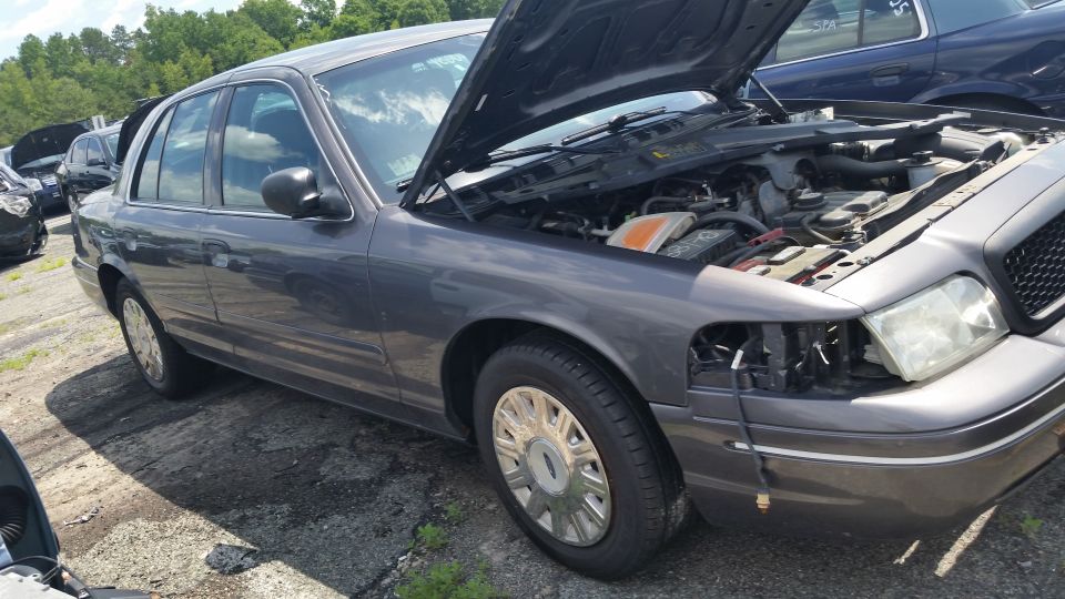 Gray Ford Crown Victoria sedan with open hood in a salvage yard