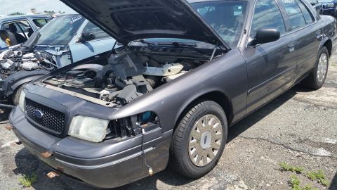 2001 Ford Crown Victoria - Photo of a gray Ford Crown Victoria sedan with hood up and front bumper cover removed at a salvage yard.