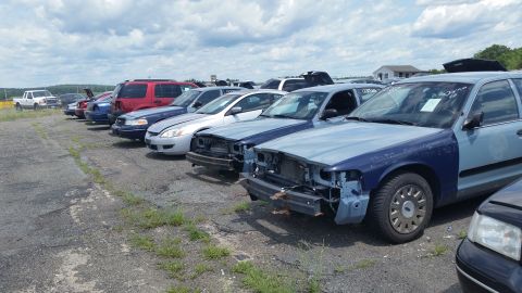 2001 Ford Crown Victoria - Photo of a line of salvage vehicles with a Ford Crown Victoria missing its front-end body panels.