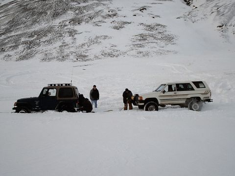 1996 Ford Bronco - Two off-road vehicles are stuck in deep snow, with individuals attempting to free them using shovels.