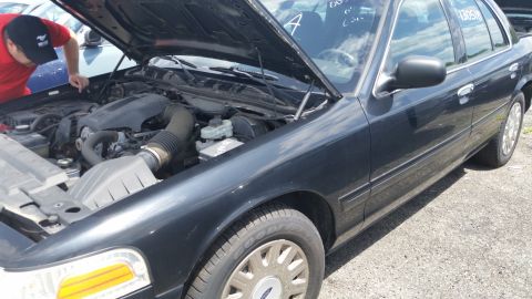 2001 Ford Crown Victoria - Photo of a person leaning into the engine bay of a Ford Crown Victoria at a salvage lot.