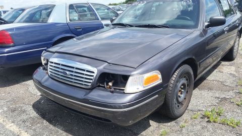 2001 Ford Crown Victoria - Photo of a gray Ford Crown Victoria with its front bumper cover removed at a salvage yard.