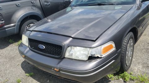 2001 Ford Crown Victoria - Photo of the front of a gray Ford Crown Victoria with a damaged headlight in a salvage yard.