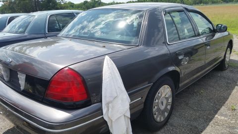 2001 Ford Crown Victoria - A dark gray 2001 Ford Crown Victoria is parked next to another vehicle, with a towel draped over its rear fender.