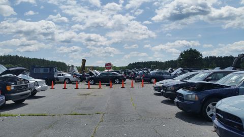 2001 Ford Crown Victoria - A lot filled with various vehicles, some with hoods open, under a partly cloudy sky.
