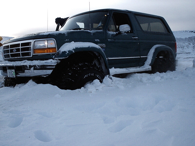 Dark green lifted Ford Bronco stuck in deep snow, front three-quarter view