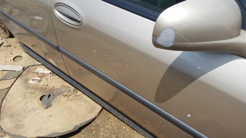 2001 Ford Crown Victoria - Side view of a tan car door and side mirror, showing damage to the mirror's paint.