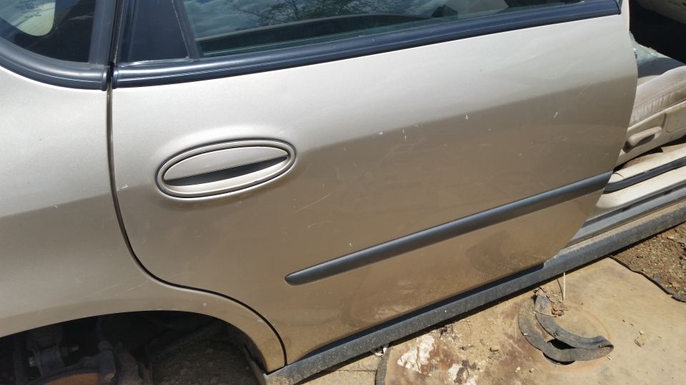 Side view of a tan car door, open to show part of the interior and a missing wheel well
