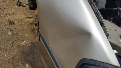 2001 Ford Crown Victoria - Dented gold fender on a vehicle, with visible damage and surrounding debris.