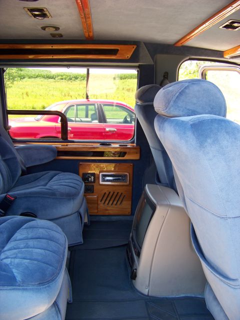2000 Ford E150 - View from inside a van shows plush seating and wood accents, with a red sedan passing by outside.