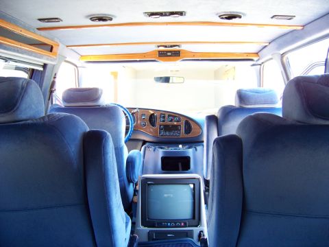 2000 Ford E150 - The interior of a van shows plush blue seats and a wood-accented dashboard with a built-in television.