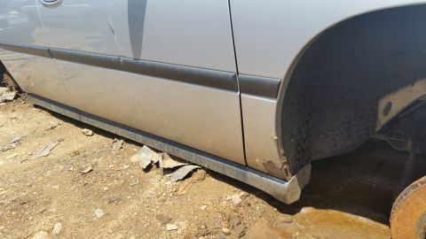 2001 Ford Crown Victoria - The side of a car, showing the lower door panel, rocker panel, and wheel well, with visible rust and dirt.