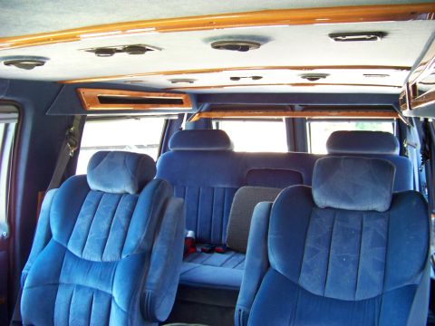 2000 Ford E150 - Interior view of a van with multiple rows of blue velour seats and wood trim accents.