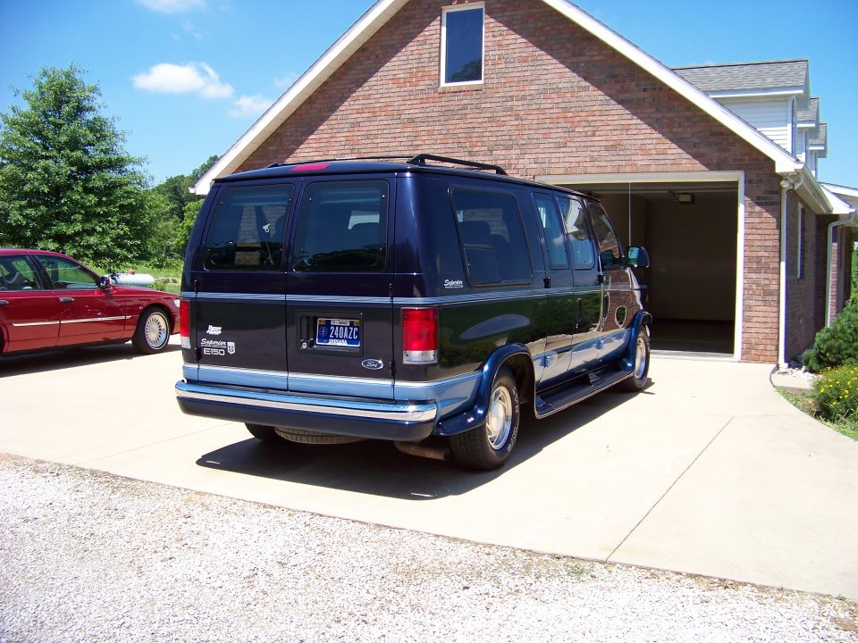 Dark blue Ford E150 van, two-tone blue trim, parked in driveway. Red sedan in background
