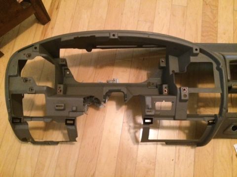 1994 Ford Bronco - Disassembled gray dashboard frame on a wooden floor. Text on a sticker reads "SUPERMOTORS www.supermotors.net".
