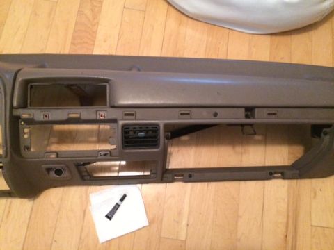 1994 Ford Bronco - Dashboard assembly removed from a vehicle, with a tube of adhesive and a cloth on the wooden floor.