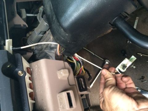 1994 Ford Bronco - A hand works on the wiring harness and fuse box inside a vehicle's dashboard.