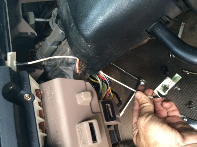 Close-up of car interior wiring harness and fuse box with a hand holding a wire connector