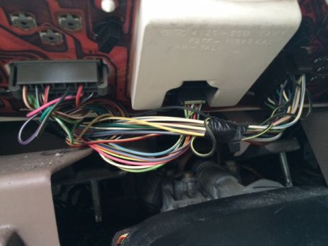1994 Ford Bronco - The complex wiring harness behind a vehicle's dashboard is visible, with part numbers on a plastic cover.